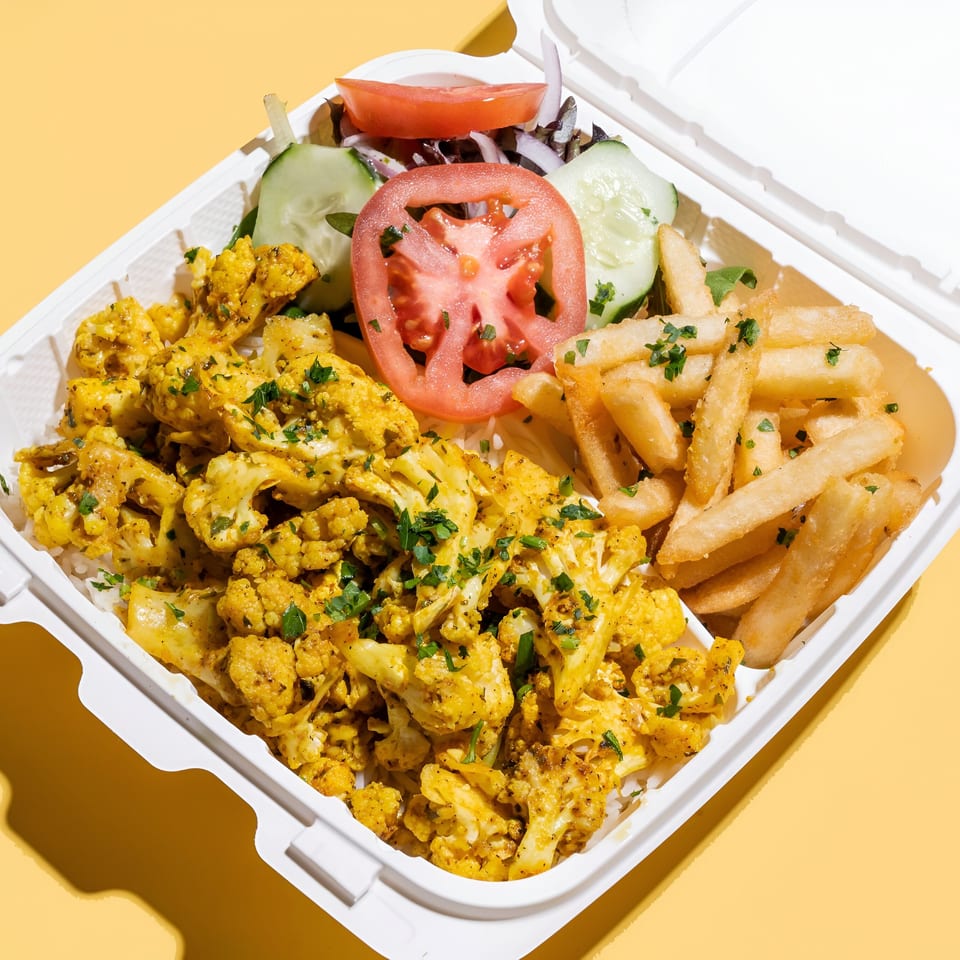 Middle-Eastern cauliflower and fries with a side salad in a white takeout container.
