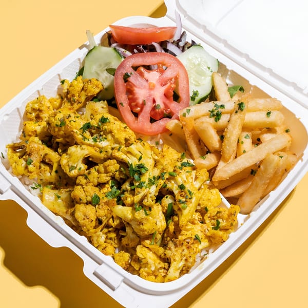 Sheesh Grill's Middle-Eastern cauliflower and rice dish with fries, tomatoes, and cucumbers in a takeout container.